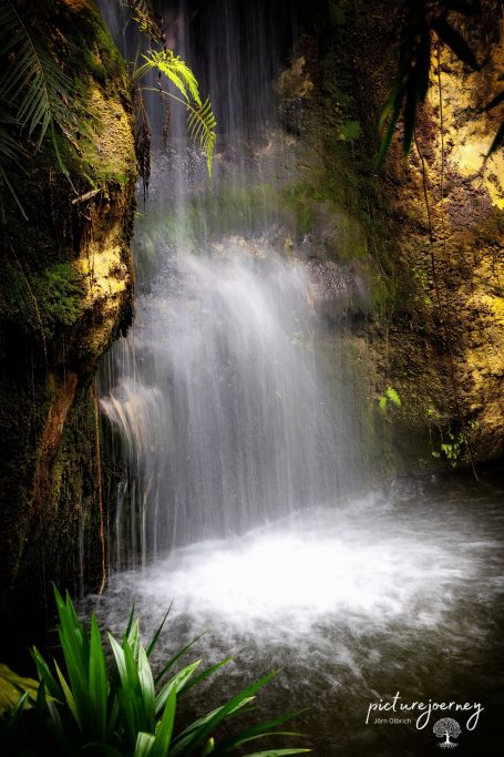 Wasserfall mit grünem Umfeld, das klares Wasser in ein ruhiges Becken fließen lässt.