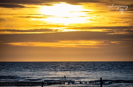Sonnenuntergang über dem Meer mit einem schwachen Silhouette von Menschen am Strand.